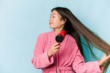 Obraz premium Young asian woman drying hair isolated on blue background