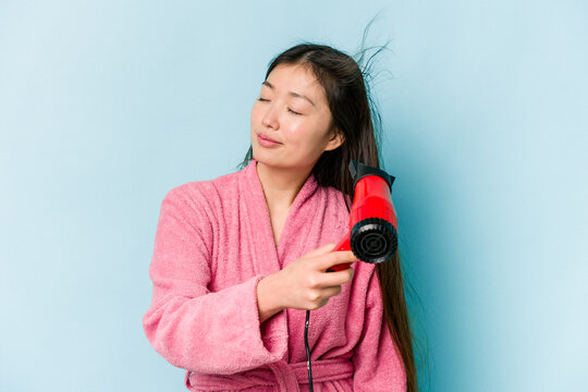 Young asian woman drying hair isolated on blue background