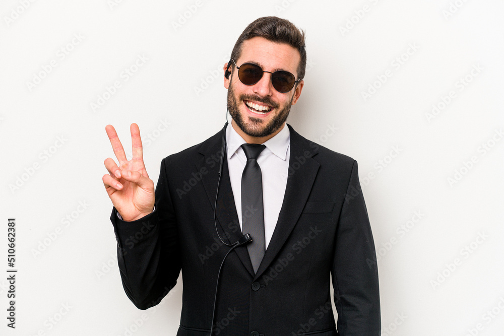 Wall mural young caucasian bodyguard man isolated on white background joyful and carefree showing a peace symbo