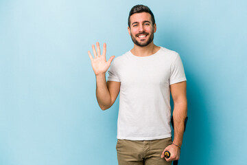 Young man with crutches isolated on blue background smiling cheerful showing number five with fingers.