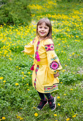 little beautiful child   in ukrainian yellow embroidery  dancing on green and yellow meadow with dandelions
