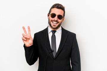 Young caucasian bodyguard man isolated on white background joyful and carefree showing a peace symbol with fingers.