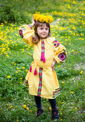 little beautiful girl  in ukrainian yellow embroidery and wreath of flowers sitting on green and yellow meadow with dandelions