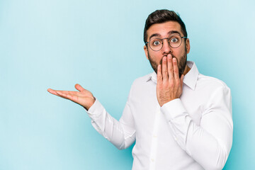 Young caucasian man isolated on blue background impressed holding copy space on palm.