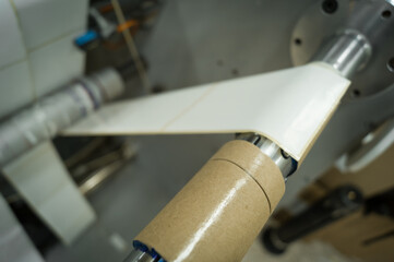 Cardboard reel on the shaft of the machine for cutting and winding tapes with self-adhesive label. Equipment in the printing house for the production of printing products. Selective focus