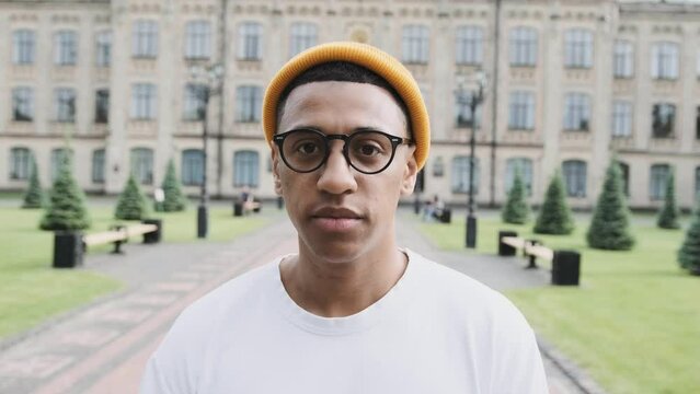 Stylish African American international student looks serious. Closeup portrait with University on the background.