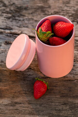 Big, juicy strawberries in a pink container on a wooden table. Beautiful, soft light of the setting sun. - 510664363