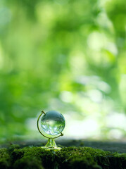 glass earth globe on abstract blurred natural green background. Concept of ecology, save nature,...