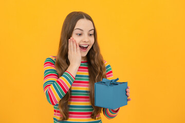 Teenager child holding gift box on yellow isolated background. Gift for kids birthday. Christmas or New Year present box. Excited face, cheerful emotions of teenager girl.