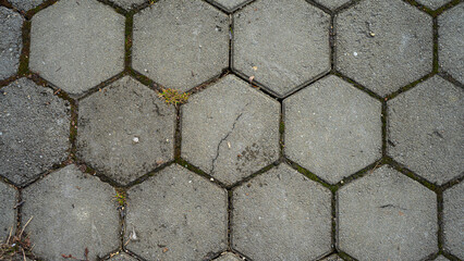 Cracked gray paving slabs in the shape of hexagons with small debris, moss and sprouted grass
