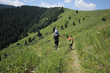 A man and a boys go hiking in the summer forest with a backpack for hiking.