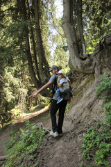 Young man with a baby in a sling behind his back walking on the road in the forest