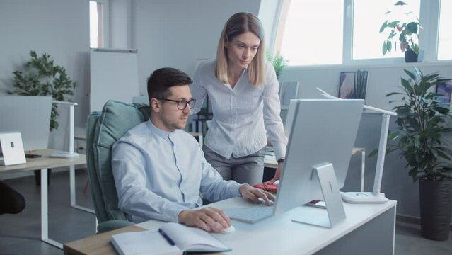 Young man and woman talking use computer working together in a modern office. On background businesspeople. Slow motion
