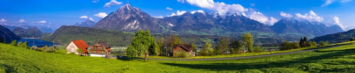 Fototapeta na wymiar Switzerland nature scenery - typical traditional village with green meadows and wooden houses near Lucerne town and lake with stunning view for Pilatus mountain