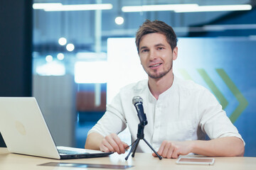Business coach in office records online book, portrait looks at camera smiling, man with...