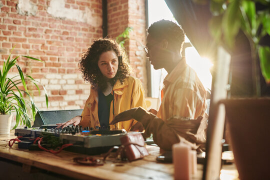 Young Woman In Casualwear Looking At Boyfriend Explaining Her How To Create New Music While Both Standing By Dj Booth In Studio