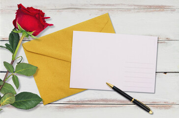 A craft envelope with an empty white postcard and a red rose on a white wooden background. Flat lay. Copy space. Mock up. The concept of Valentine's Day, Birthday and wedding invitation