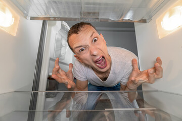 Hungry person is looking for food in refrigerator and is in shock. An empty refrigerator. guy is upset, screams and breaks down. Crisis and lack money. family starving. depression of man without money