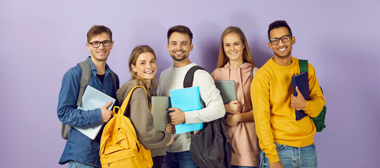 Fototapeta Diverse group of smiling university or college students. Happy multi ethnic young friends in casual wear with backpacks, class textbooks and modern laptop PCs standing together and looking at camera obraz