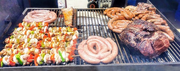 barbecue being made on embers of wood logs. on top of the grill there are: sausages, loin, ribs, and skewers of bell pepper and mushroom with pieces of meat. 