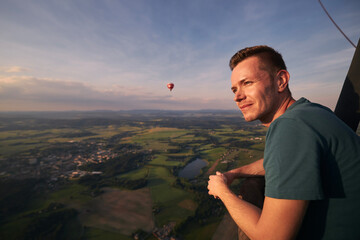 Man enjoying view from hot air balloon during flight over beautiful landscape at sunset. Themes...