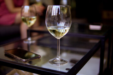 champagne glasses on glass table next to a cell phone at a casual event with unrecognizable people in the background