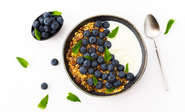 Homemade granola with yogurt, blueberries and mint leaves in a bowl on a white background, delicious healthy breakfast