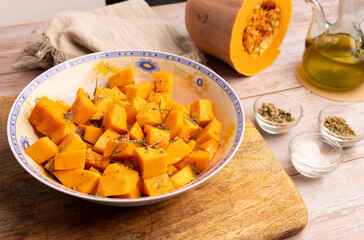 Diced pumpkin pieces in a bowl, with spices and olive oil