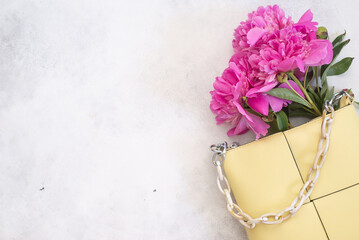 Flat lay of women handbag and pink peonies on a light gray background. Empty space for text. Woman consept.