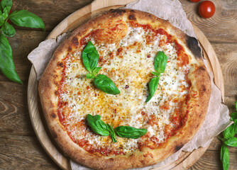 A whole margarita pizza lies on a round board, top view. Nearby lies a basil