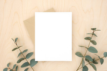 Blank greeting card, invitation mockup. Eucalyptus branches plant on wooden table background. Flat lay, top view. Copy space. Canvas mock up. Modern Minimal business brand template. Soft shadow