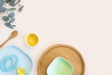 Baby accessories and tableware for food on beige background. First feeding for kids concept. Flat lay, Top View, Space for text. Silicone dishware, bib, cup on neutral backdrop. Serving baby food