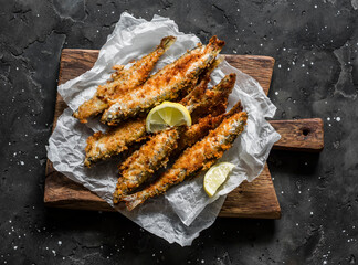 Delicious tapas, appetizer - sardines fried in bread crumbs on a cutting board on a dark background, top view