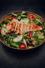 Colorful mixed salad of cucumber, cherry tomatoes and arugula with roasted chicken breast in a bowl in portrait format