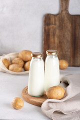 Vegan plant based milk in two glass bottles. Alternative potato milk and potato tubers on gray table