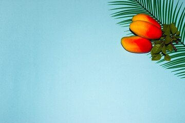 three mangoes on a palm leaf in the upper right corner of a blue background, creative summer...