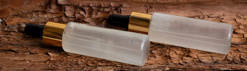 Vials of serum with a pipette lie against a background of brown bark. A close-up of a frosted glass container for a cosmetic skin care product.