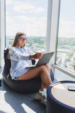 Smiling female student in glasses enjoying watching movie online on laptop in free time in cozy coworking space, happy female freelancer chatting with friend on social media, sharing profile photos