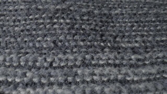 Knitted gray wool fabric in macro. Structure of warm garment, sweaters, cozy plaid, bedspreads, scarf. Knitted soft material made of wool. Background from knitted textile. Extreme close up of fluffy