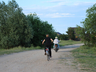 Obraz premium Young people ride a motorcycle and bicycle on the road on the outskirts of the village on a summer evening