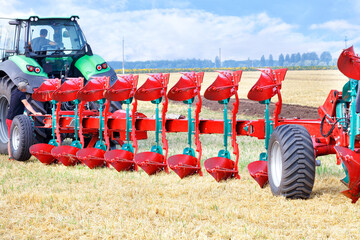 Red plow as a trailer on a tractor on the background of an agricultural field.