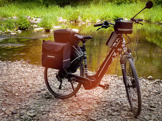 Ein E Bike mit vielen Taschen steht am Ufer des Flusses Ruhr in Deutschland. Eine schöne Tour mit viel Gepäck. Modernes E Bike mit Sternen und Streifen. - obrazy, fototapety, plakaty