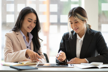 Two Asian business women working together using digital tablets discussing new startup project ideas. Analyze the planning and statistics of the financial and investment markets at the office.