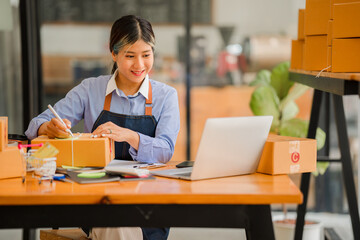 Asian women SME small business entrepreneurs online selling ideas Happy Young Asian business owner working on computers and boxes at home. Deliver SME parcel boxes to customers horizontally	