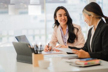 Two Asian business women working together using digital tablets discussing new startup project ideas. Analyze the planning and statistics of the financial and investment markets at the office.