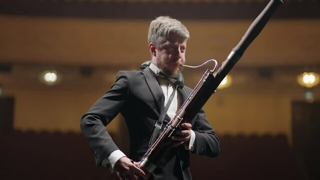 talented musician is playing bassoon in scene of music hall in evening, rehearsal of symphonic orchestra