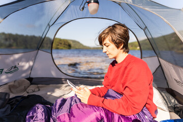 Portrait of a woman sitting inside her tent while camping in front of a lake in Scotland
