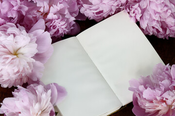 Notebook with blank paper pages among pink peony flowers. Spring stationery mockup.