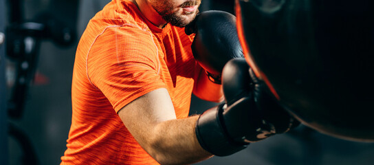 Male bearded boxer punching in boxing bag in gym
