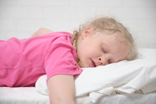 cute little girl with blond hair and a pink t-shirt sleeps on a white bed
